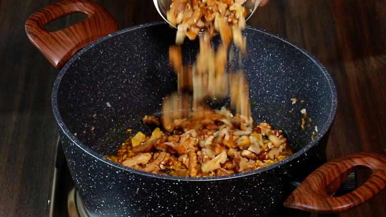 Roasted California walnut kernels arre being added to a grey and white speckled non stick pan with two large wooden handles on an electric stove - Malvani Green Peas and Walnut Curry Recipe